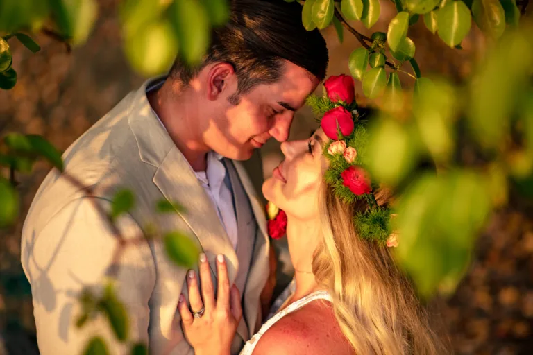 Couple embracing among tropical leaves, the bride with a red flower in her hair
