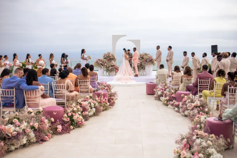 Guests seated for a ceremony with pink floral aisle by the sea