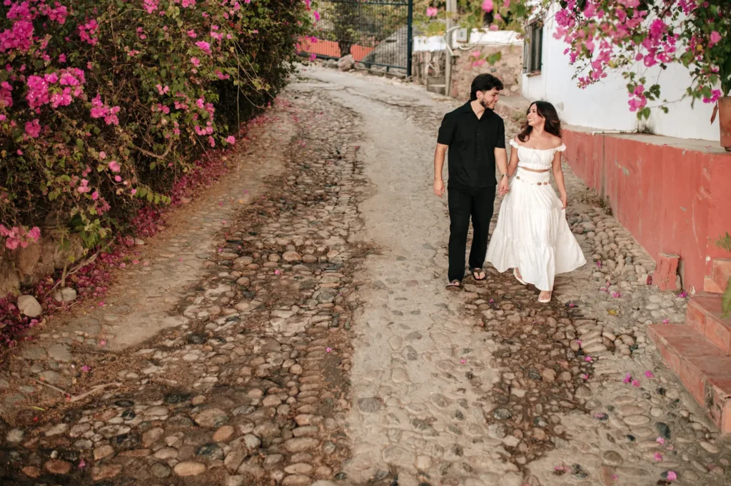 Couple walking down a dirt road lined with bougainvillea